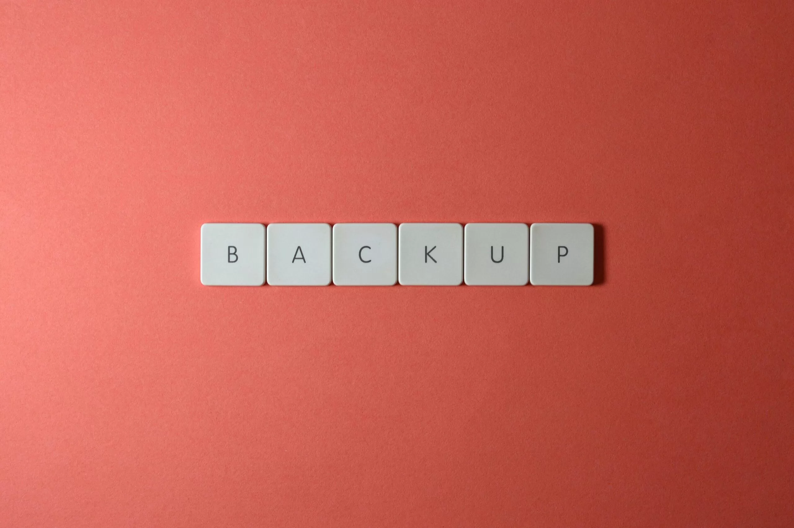 Free Close-up of keyboard keys spelling 'BACKUP' placed on a coral-colored surface. Stock Photo