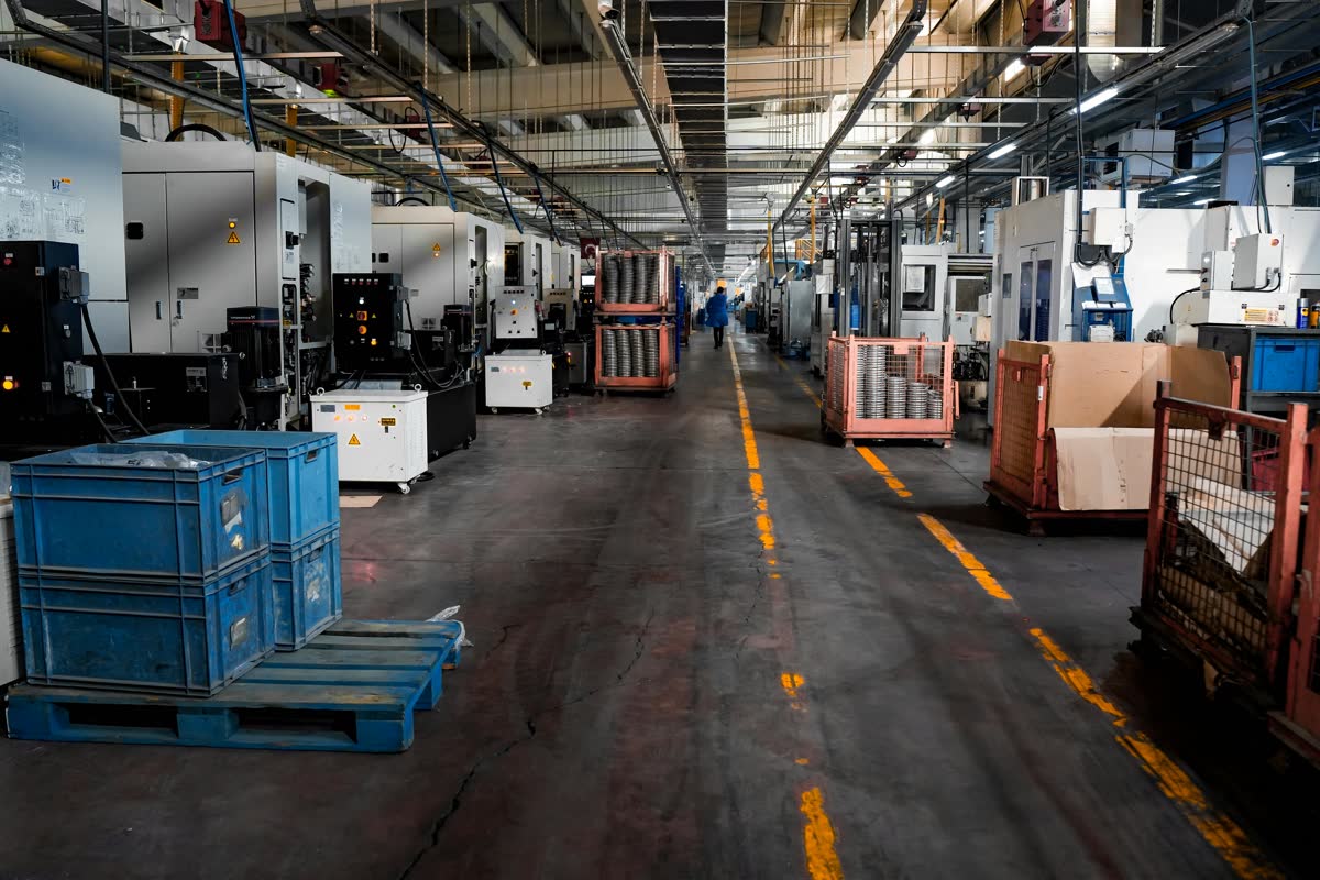 Manufacturing Equipment Obsolescence Planning -- CNC precision machining shop floor with rows of enclosed machining centers, all requiring IT and OT asset documentation